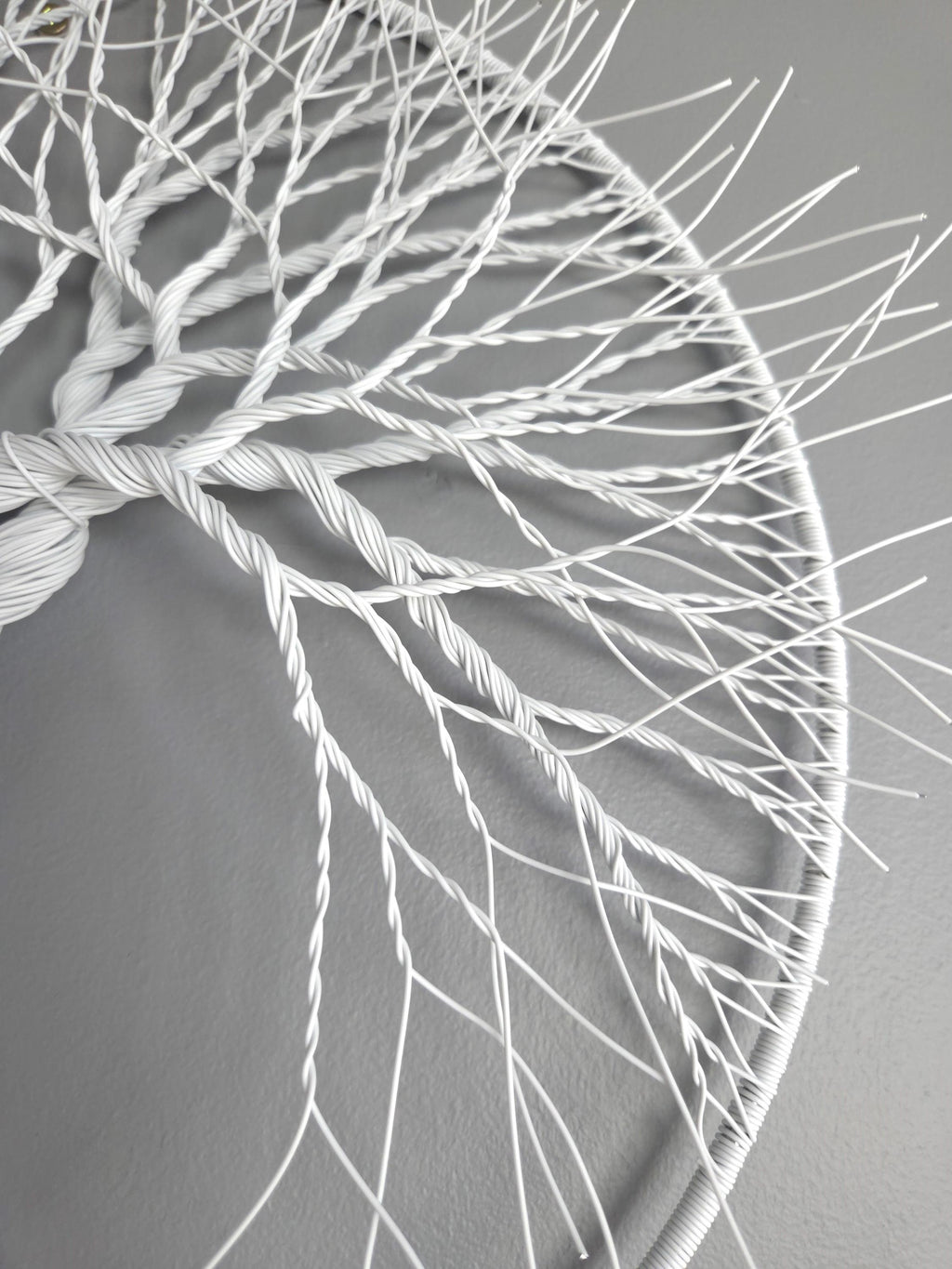 Close-up of a white woven circular art piece on a gray background