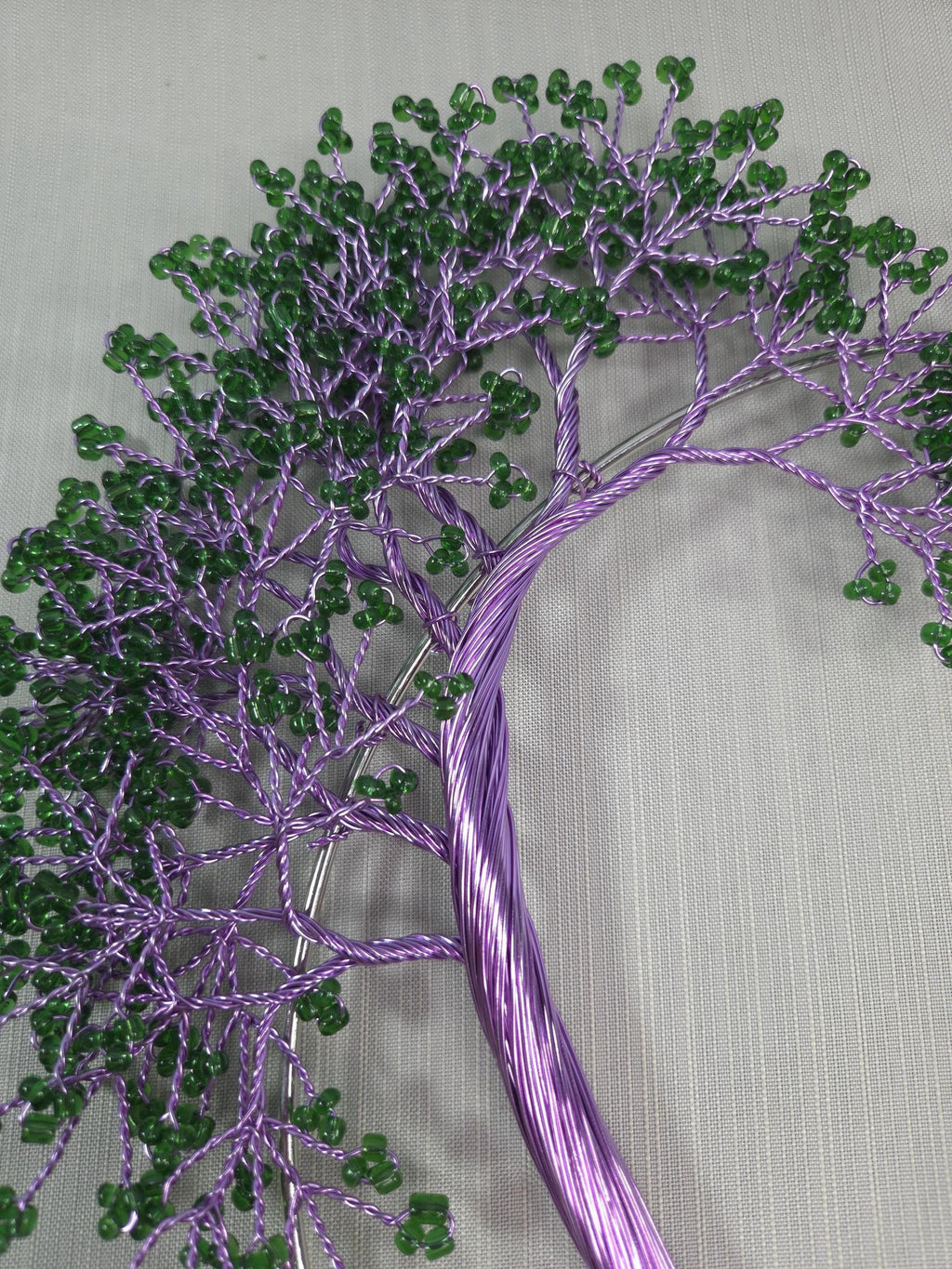 Embroidered tree design with green beads on a purple thread against a light gray background