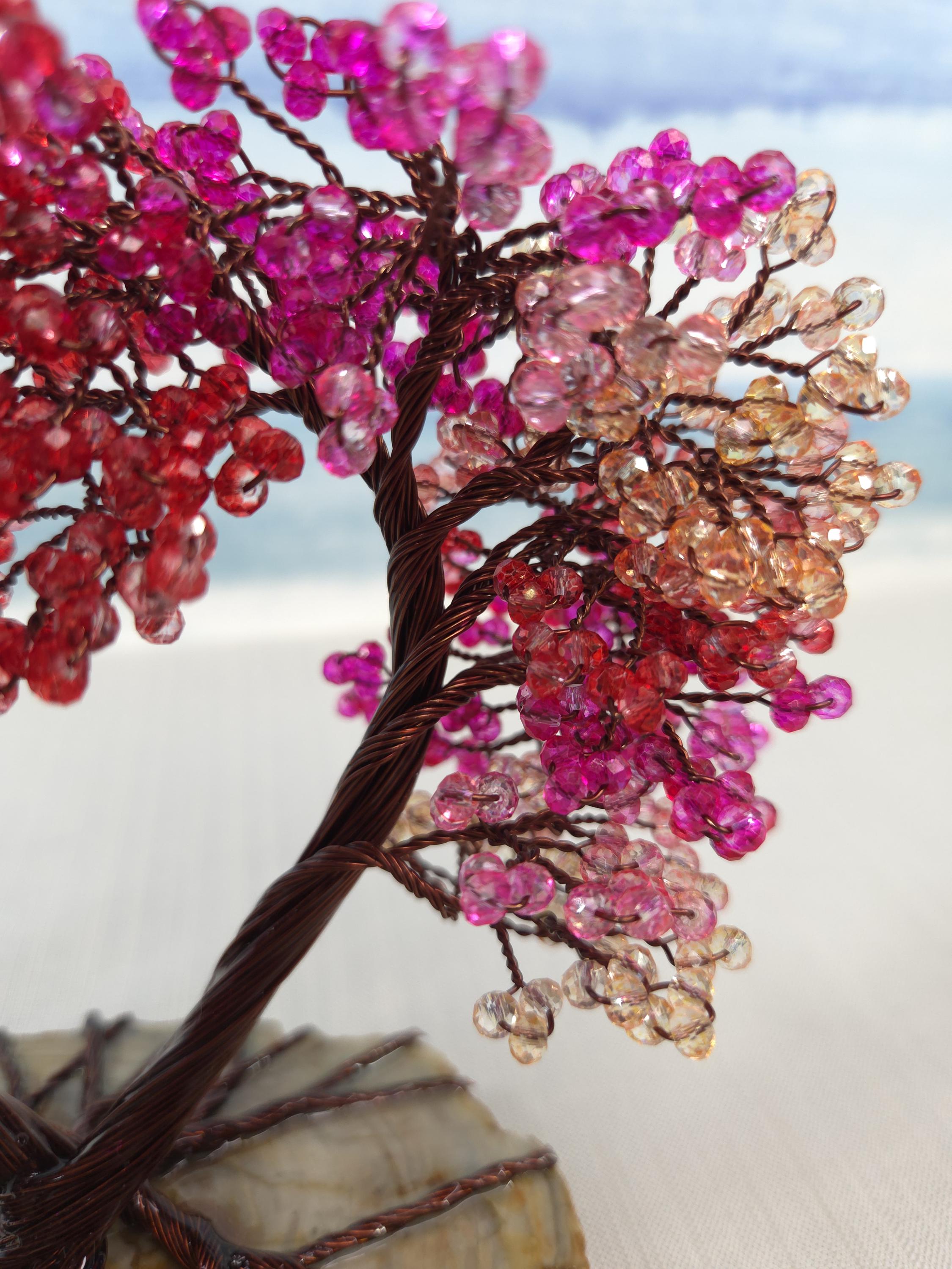 Decorative tree made of beaded branches with pink, red, and brown beads against a light background.