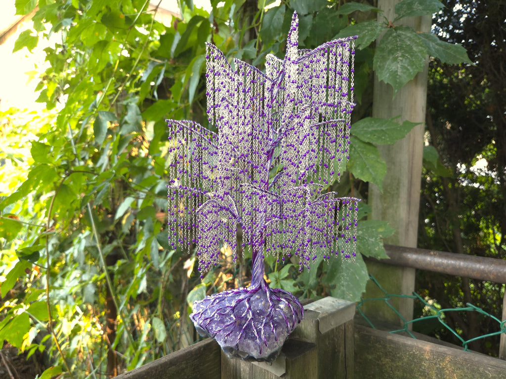 Decorative purple beaded tree sculpture on a wooden platform with green foliage in the background