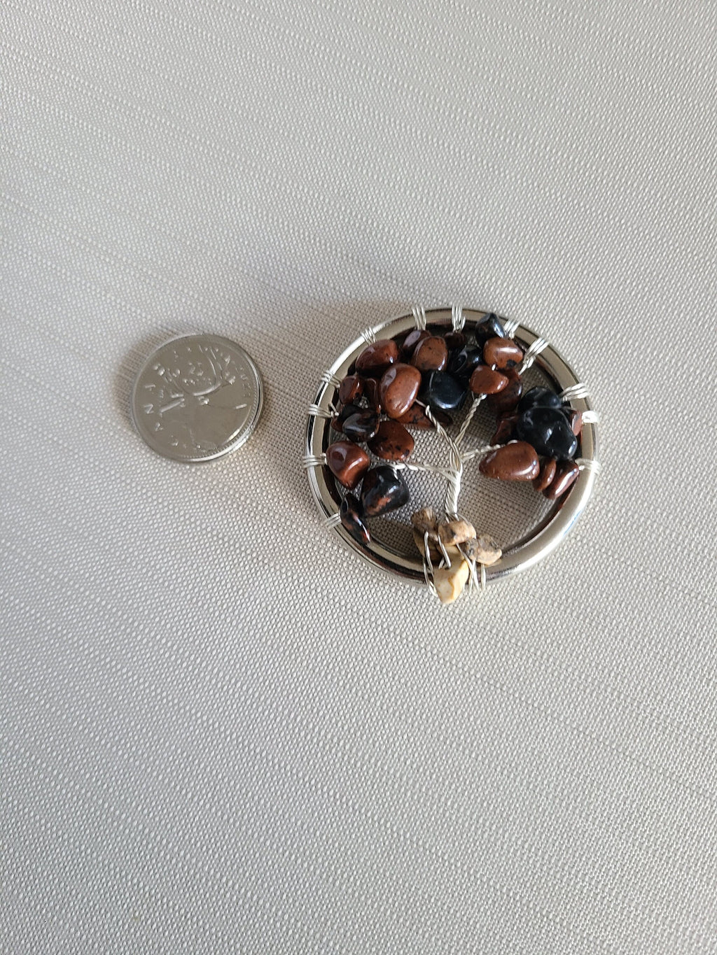 Small circular object with stones on a gray surface next to a coin for scale.