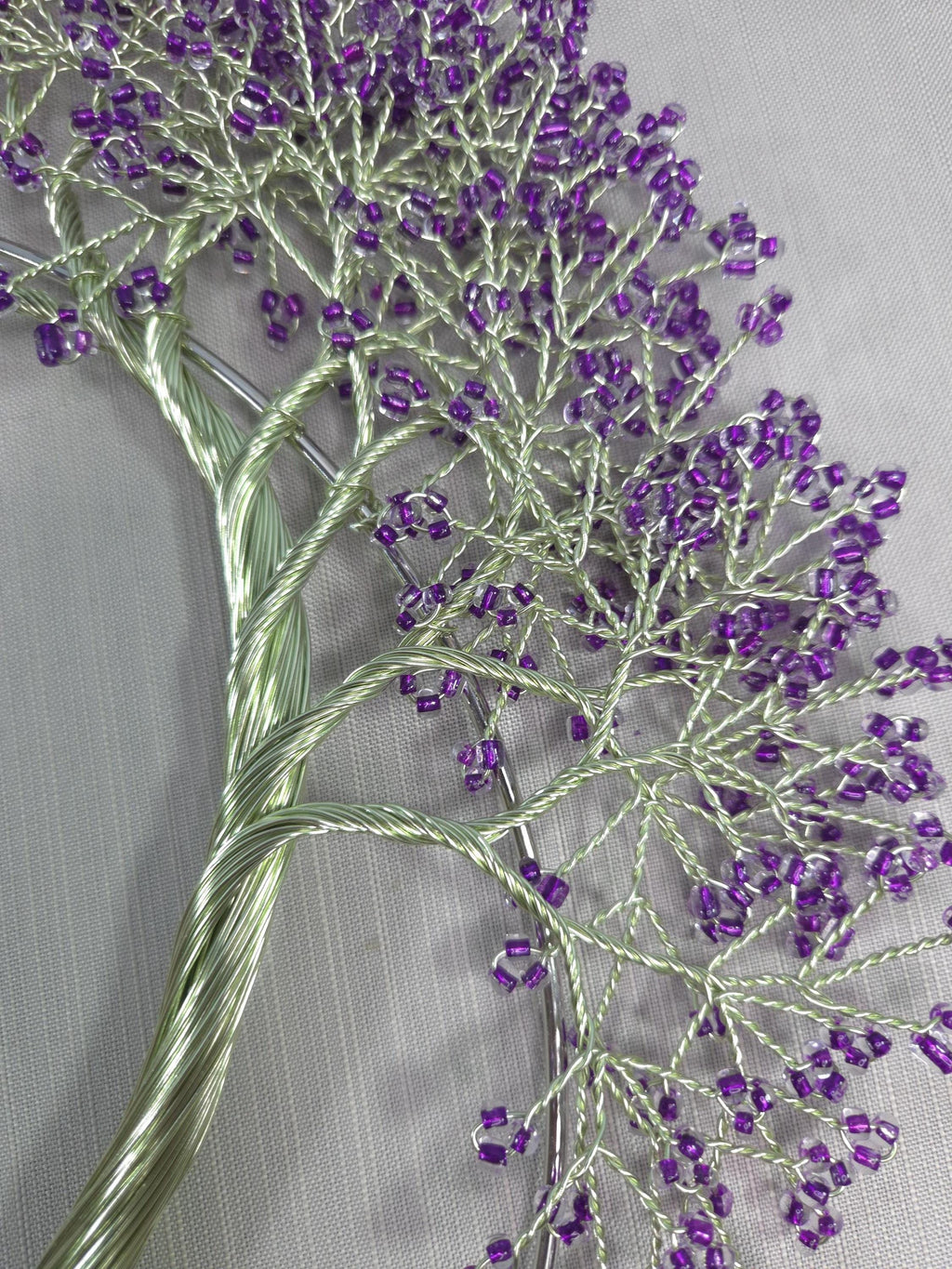 Close-up of embroidered branch with purple beads on a gray fabric background
