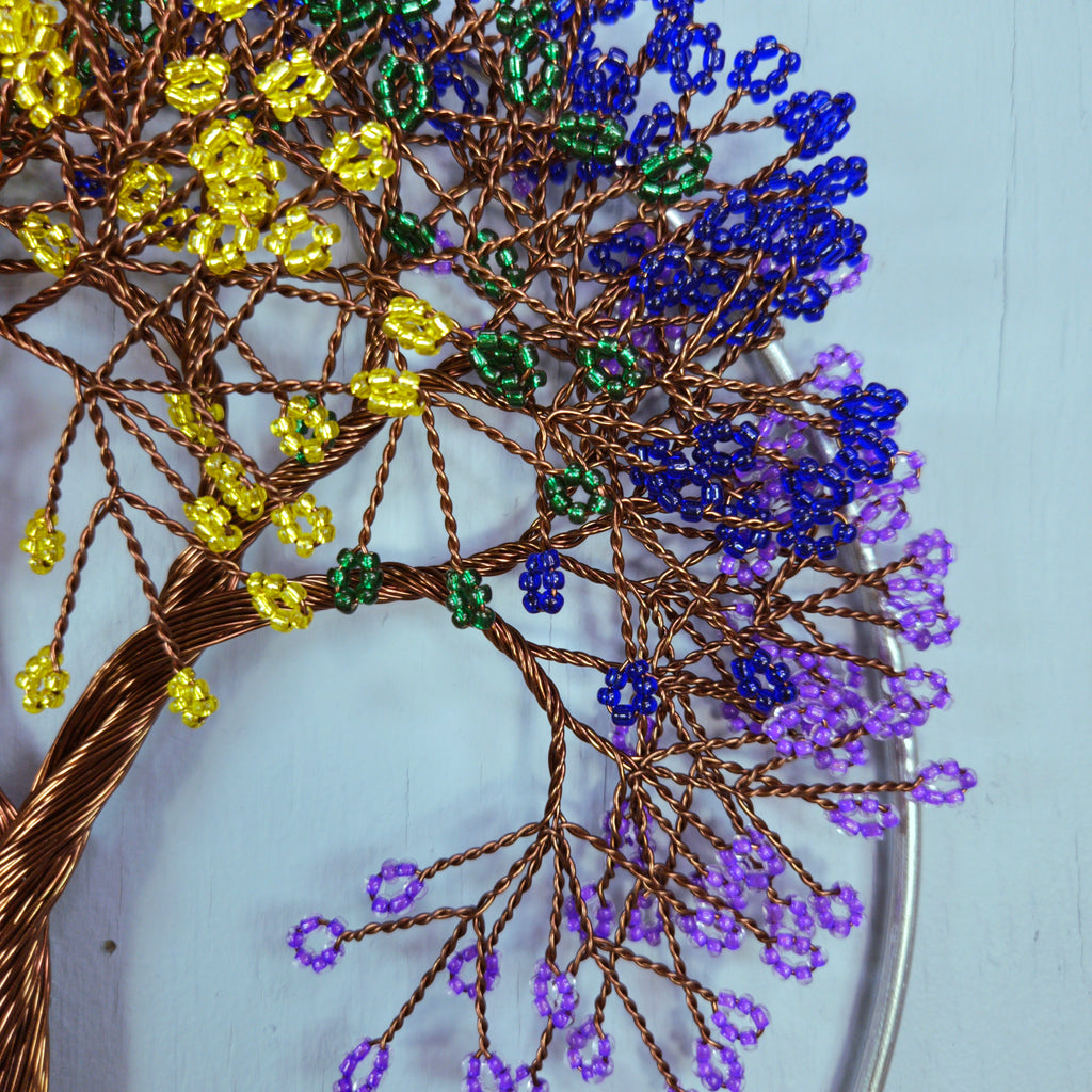 Close-up of a beaded tree with yellow, blue, and purple beads on a white background